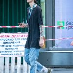 Фотография мужчины с татуировками на руке, идущего по улице. Современный стиль одежды, солнечный день.