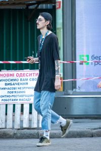 Фотография мужчины с татуировками на руке, идущего по улице. Современный стиль одежды, солнечный день.