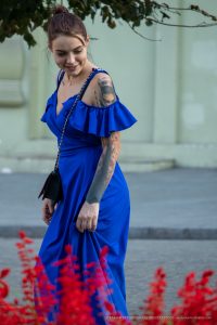 Фото тату на руке и шее женщины в синем платье, смотрящей в сторону. Детализированный рисунок татуировки, стиль стрит-арт.