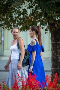Фото тату на руке и шее девушки в синем платье, смотрящей в сторону. Детализированный рисунок татуировки, стиль стрит-арт.