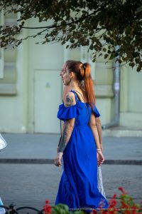 Фото тату на руке и шее девушки в синем платье, смотрящей в сторону. Детализированный рисунок татуировки, стиль стрит-арт.