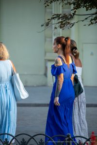 Фото тату на руке и шее девушки в синем платье, смотрящей в сторону. Детализированный рисунок татуировки, стиль стрит-арт.