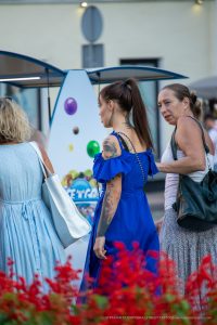 Фотография девушки с татуировками на плече и шее, идущей по улице в синем платье. Вид сзади, акцент на татуировках.