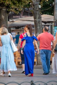 Фото тату на плече и шее девушки в синем платье, идущей по улице. Вид сзади, демонстрирующий детали рисунка татуировки.