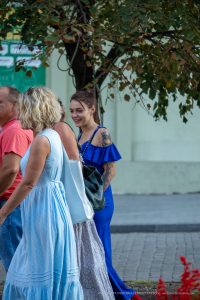 Фотография девушки в синем платье, демонстрирующая татуировки на руке, включая изображение птицы и цветочные узоры.