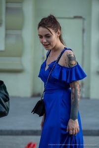 Фотография девушки в синем платье с видимыми татуировками на руке, включая изображение птицы и цветочные узоры.