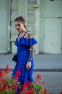 Фото тату на руке девушки в синем платье. Изображены детализированные рисунки, включая птицу и цветочные мотивы.