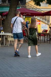Фотография мужчины с татуировкой на ноге, фотографирующего девушку на улице. Татуировка в японском стиле, вид сзади.