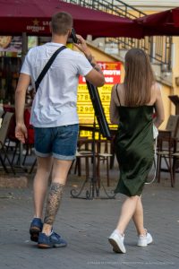 Фотография мужчины с татуировкой на ноге и девушки в зеленом платье, идущих по улице. Татуировка в японском стиле, вид сзади.