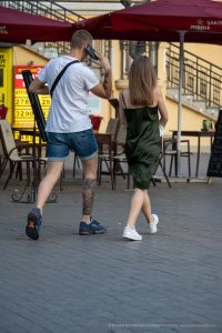 Фотография мужчины с татуировкой на ноге, фотографирующего девушку на улице. Татуировка в японском стиле, вид сзади.