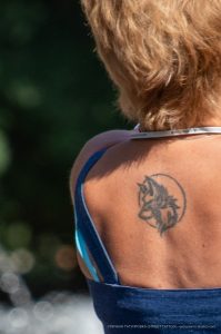 Фото тату на лопатке: стилизованный волк в круге, выполненный в технике дотворк. Черный рисунок татуировки на женской коже.