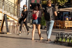Фото тату на щиколотке девушки, идущей по улице. Небольшой рисунок татуировки в виде абстрактного символа, выполненный в черном цвете.