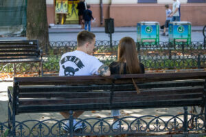 Фото парня с татуировкой на руке и девушки, сидящих на скамейке в парке. Видна часть татуировки на предплечье.