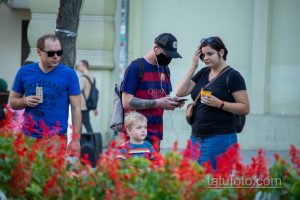 Фото мужчины в футболке, кепке и с татуировкой розы и черепа на руке. Черно-белый рисунок татуировки в стиле реализм.