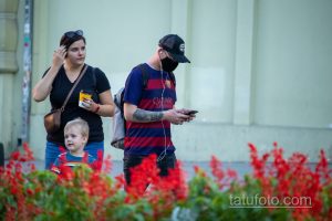 Фото мужчины в футболке, кепке и с татуировкой розы и черепа на руке. Черно-белый рисунок татуировки в стиле реализм.