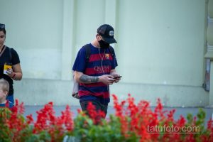 Фото мужчины в футболке, кепке и с татуировкой розы и черепа на руке. Черно-белый рисунок татуировки в стиле реализм.