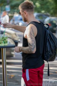 Фото тату розы на плече мужчины, выполненное в реалистичном стиле с использованием черных и серых оттенков. Мужчина указывает пальцем в сторону.