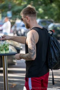 Фото тату розы на плече мужчины, выполненное в реалистичном стиле с использованием черных и серых оттенков. Мужчина держит сигарету.