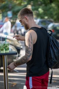 Фото тату розы на плече мужчины, выполненное в реалистичном стиле с использованием черных и серых оттенков. Вид сбоку, мужчина курит.