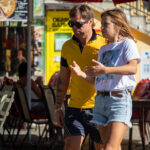 Фото мужчины с татуировкой на руке, одетого в желтую рубашку и шорты. Рисунок татуировки выполнен в ярких цветах и имеет сложную структуру.