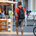 Фото тату на теле мужчины: детализированные рисунки на руках и спине, на фоне городской улицы и велосипеда.