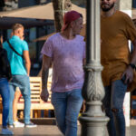 Фото мужчины с татуировкой на руке, одетого в розовую футболку и кепку. Рисунок татуировки выполнен в черных тонах и имеет сложную структуру.