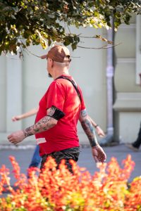 Фото тату на руке мужчины: детализированные рисунки в стиле олдскул и традиционные мотивы, покрывающие предплечье и плечо, на фоне цветущих растений.
