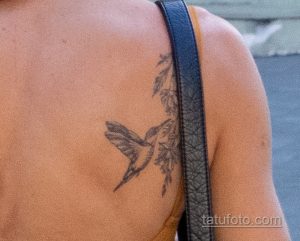 Фото тату колибри на плече. Детализированный рисунок татуировки с изображением летящей птицы и цветочных элементов.