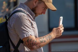 Фото тату на руке мужчины в кепке, смотрящего в телефон. Вид сбоку, акцент на детализации рисунка и его расположении.