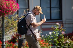 Фото тату на руке мужчины в кепке, смотрящего в телефон. Вид сбоку, акцент на детализации рисунка и его расположении.