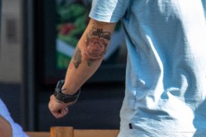 Фото татуировки розы и надписи "Selfless" на предплечье. Красная роза с зелеными листьями и черная надпись.