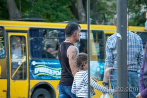 Фото мужчины с татуировкой на плече, изображающей детализированный рисунок, виднеющийся на фоне городского пейзажа.