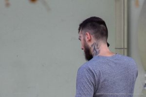 Фото тату на шее и руке мужчины с бородой. Вид сбоку, акцент на детализации рисунка и его расположении на теле.