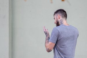 Фото тату на руке и шее мужчины, смотрящего в сторону. Вид сбоку, акцент на детализации рисунка и его расположении.