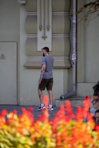 Фото тату на плече и руке мужчины, стоящего на фоне здания. Вид сзади, акцент на детализации рисунка и его расположении.