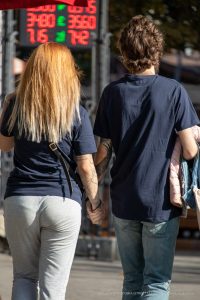 Фото тату на руке мужчины с изображением орла и части татуировки на руке женщины. Пара держится за руки на фоне городской улицы.