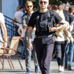 Фотография мужчины в черной одежде и кепке, с татуировками на предплечье и кисти. Он идет по улице, привлекая внимание своим стилем.