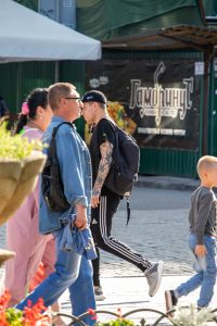 Фото тату на руке мужчины, разговаривающего с другими людьми. Рука покрыта детализированным рисунком татуировки в стиле олдскул. Мужчина одет в черную кепку и спортивный костюм.