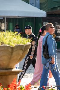 Фото тату на руке мужчины, идущего по улице в компании других людей. Рука покрыта детализированным рисунком татуировки в стиле олдскул. Мужчина одет в черную кепку и футболку.