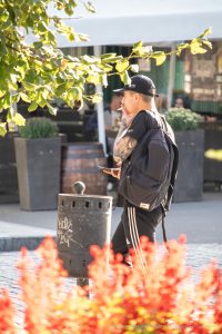 Фото тату на руке мужчины, идущего по улице с рюкзаком. Рука покрыта детализированным рисунком татуировки в стиле олдскул. Мужчина одет в черную кепку и спортивный костюм.