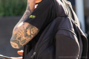 Фото крупным планом татуировки на руке мужчины. Рисунок выполнен в стиле олдскул с использованием черных и серых оттенков. Видны изображения черепов, роз и других символов.