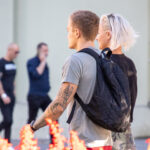 Фото мужчины с татуировкой на руке и блондинки, стоящих рядом. Видна часть татуировки с изображением ворона и деревьев. Идеи для тату.