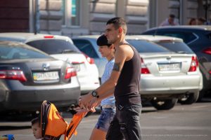Фотография мужчины и женщины с татуировками на руках, гуляющих с ребенком. Видны фрагменты рисунков на предплечьях. Уличная фотография тату.