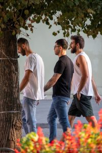 Фотография трех мужчин, идущих по улице, у одного из которых видны татуировки на руках и плечах.