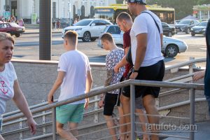 Фото мужчины с татуировкой в виде рукава на руке, стоящего в толпе людей на улице. Татуировка выполнена в технике blackwork.