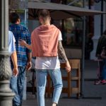 Фото мужчины с татуировкой на руке, идущего по улице. Татуировка выполнена в современном стиле с использованием черных линий и геометрических форм.
