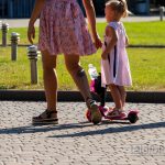 Фото татуировки на ноге женщины, частично видимой из-под одежды, в то время как она идет рядом с ребенком на самокате.