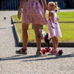 Фото татуировки на ноге женщины, частично видимой из-под одежды, в то время как она идет рядом с ребенком на самокате.