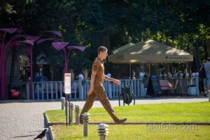 Фото тату на предплечье мужчины, идущего по парку. Татуировка выполнена в темных тонах, видны детализированные узоры и линии.