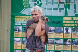 Фото тату на руке: крупный план татуировки с изображением черепа, украшенного цветами и листьями. Выполнена в черно-серых тонах с высокой детализацией.